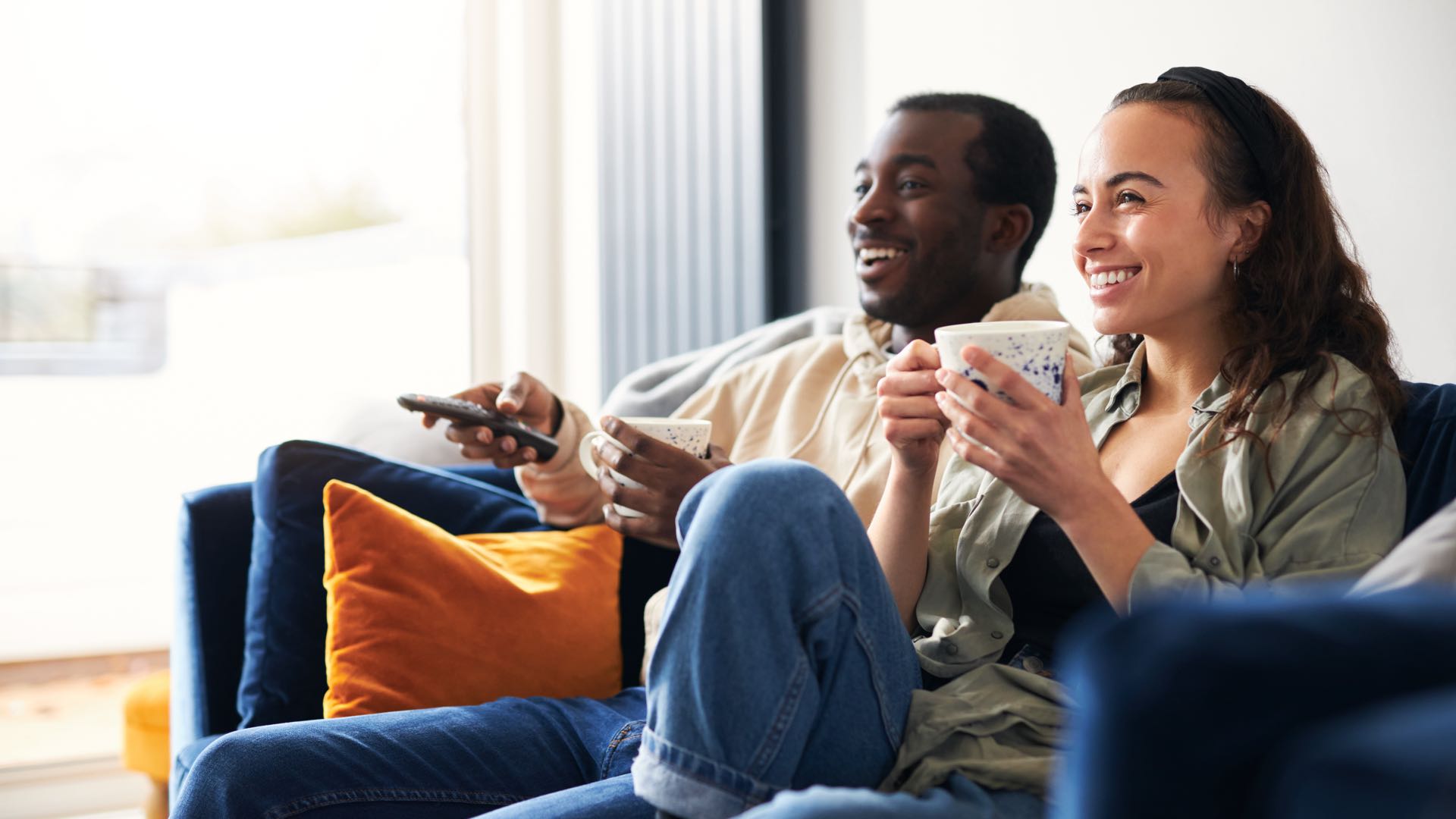 Smiling young couple relaxing at home sitting on sofa watching on-demand TV together.