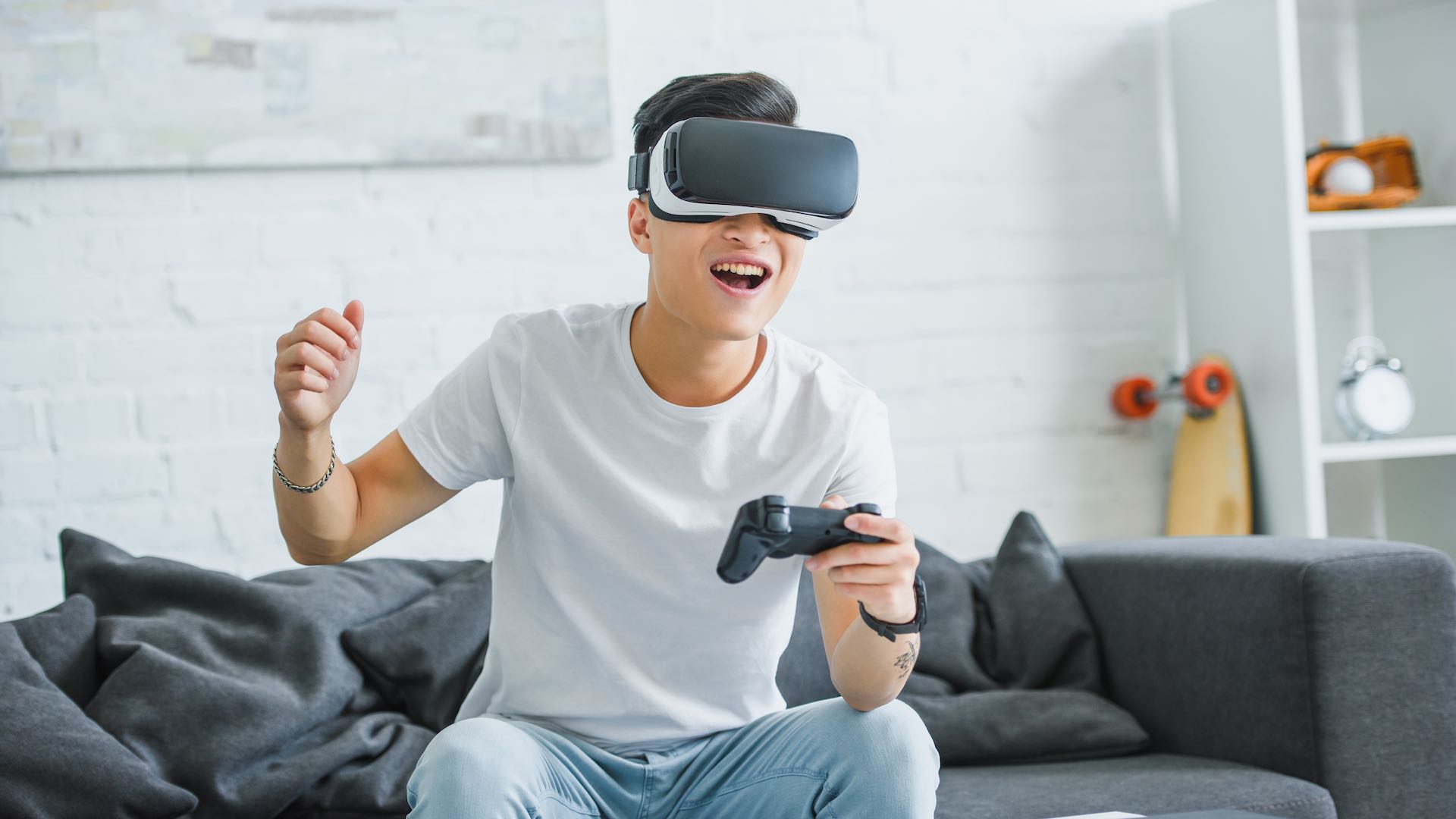 Happy young man in virtual reality headset playing with joystick at home stock photo.