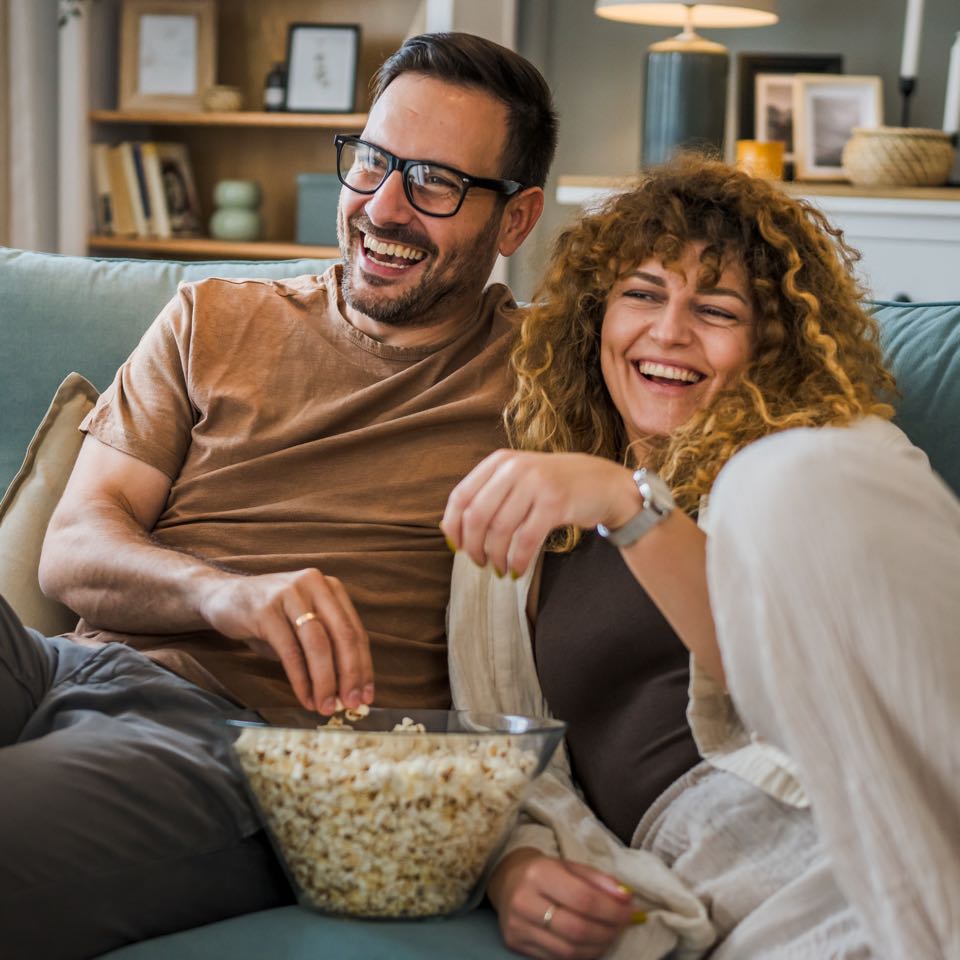 Couple sit at home on sofa bed streaming TV with Sonic Fiber Internet.