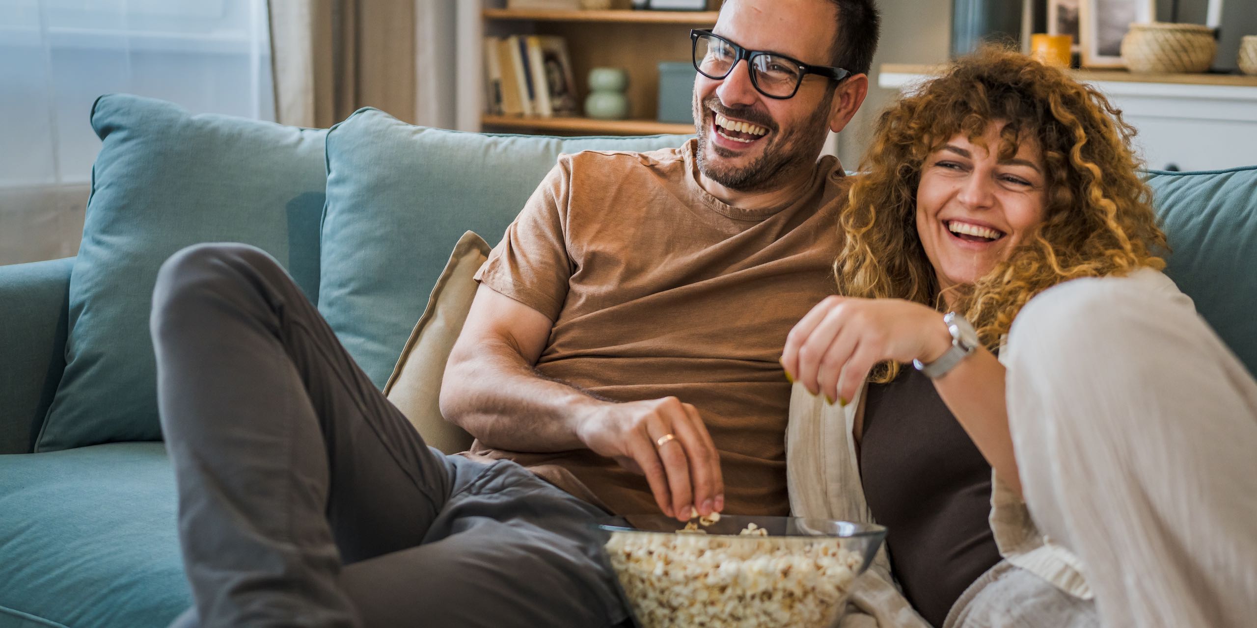 Couple sit at home on sofa bed streaming tv with Sonic Fiber Internet.