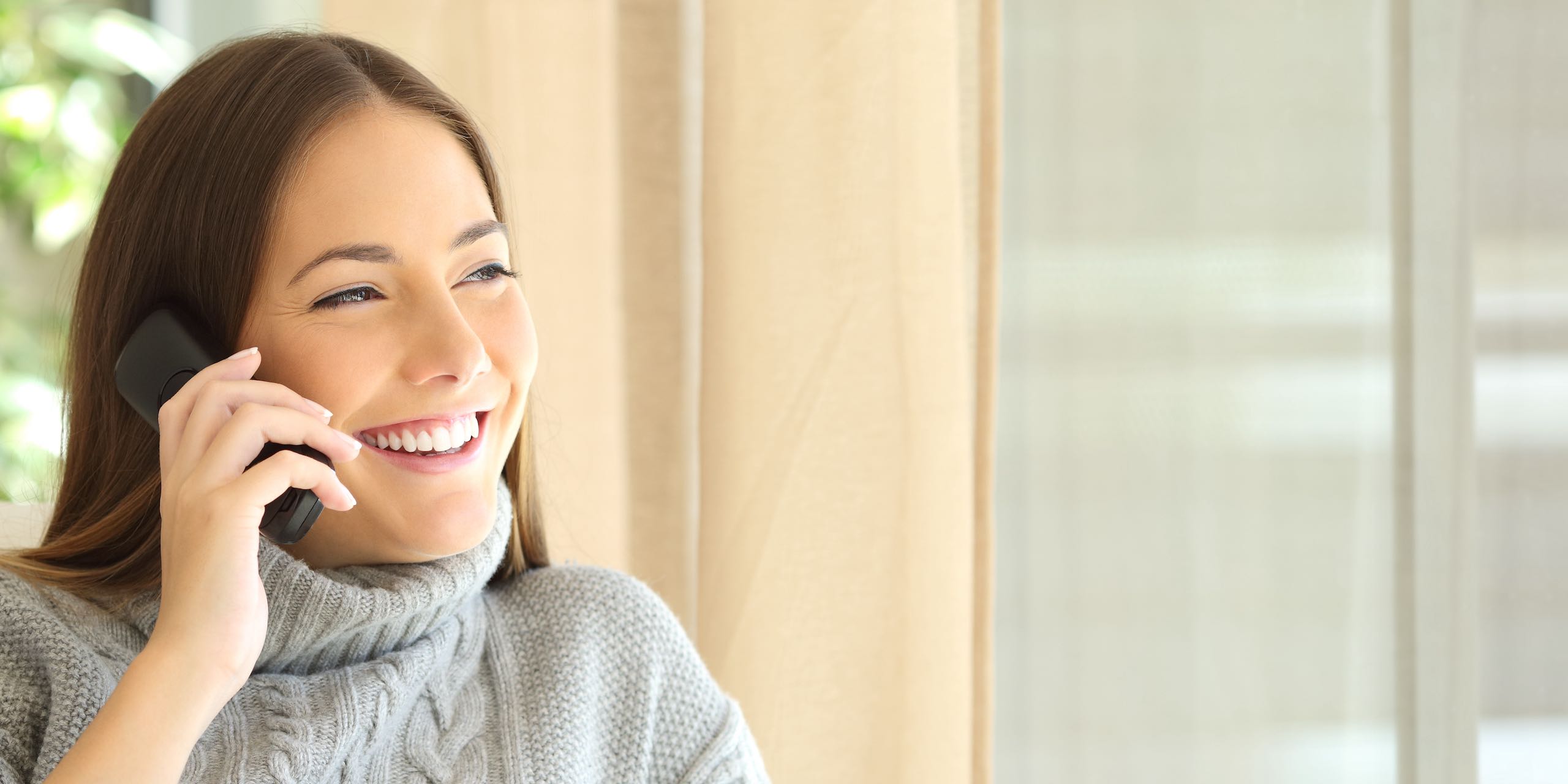 Woman talking on a land line phone sitting on a sofa in the living room at home